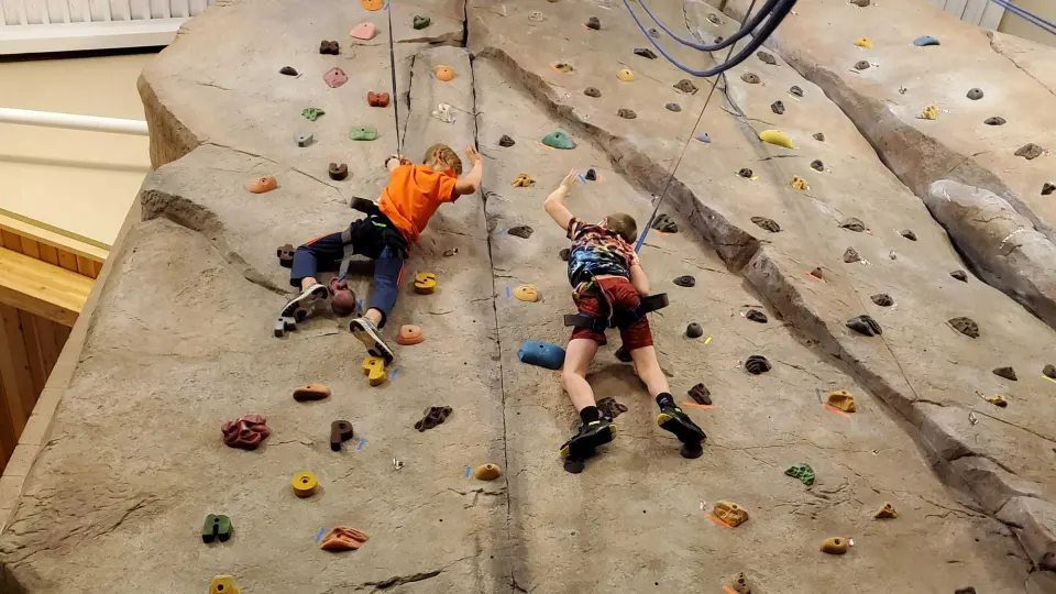 Two young climbers on top ropes on the rock-textured wall, seen from above