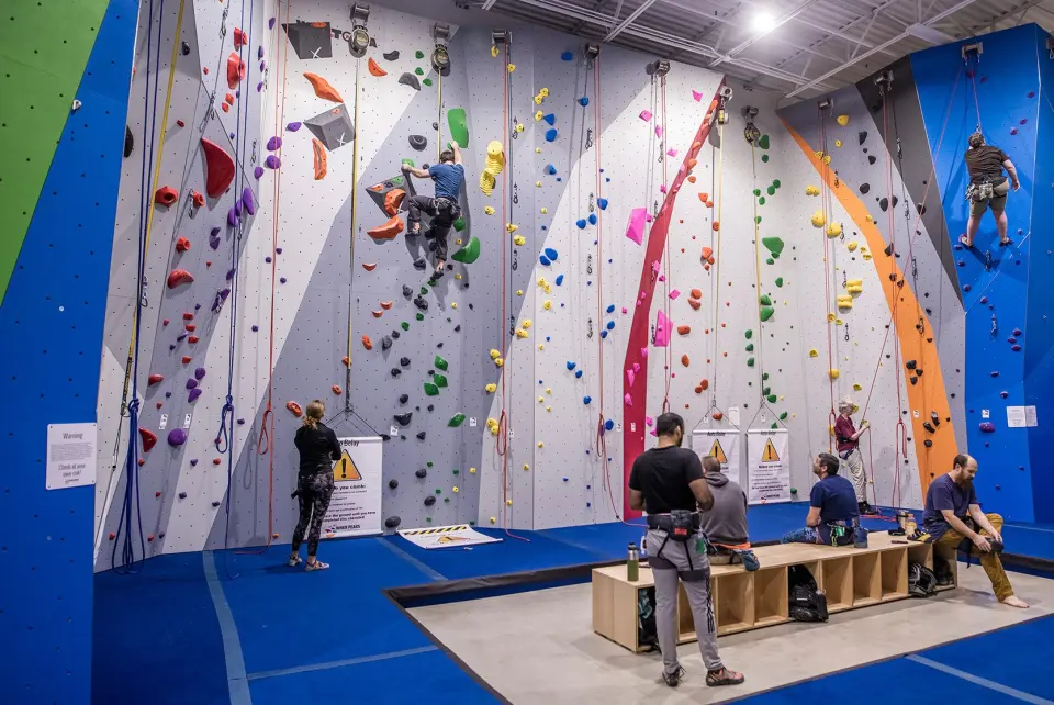 Climbers on the tall roped walls above the blue floor of the rope area