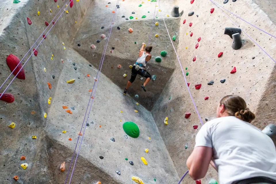 Climber high on a textured top-rope wall with a belayer below