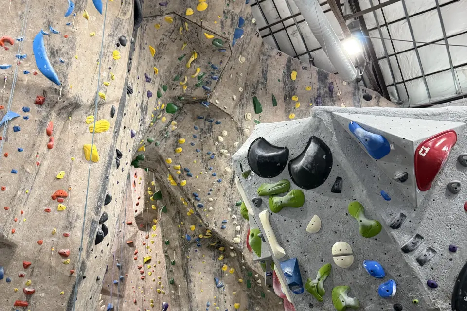 Tall roped walls beside a grey boulder with green, black and blue holds
