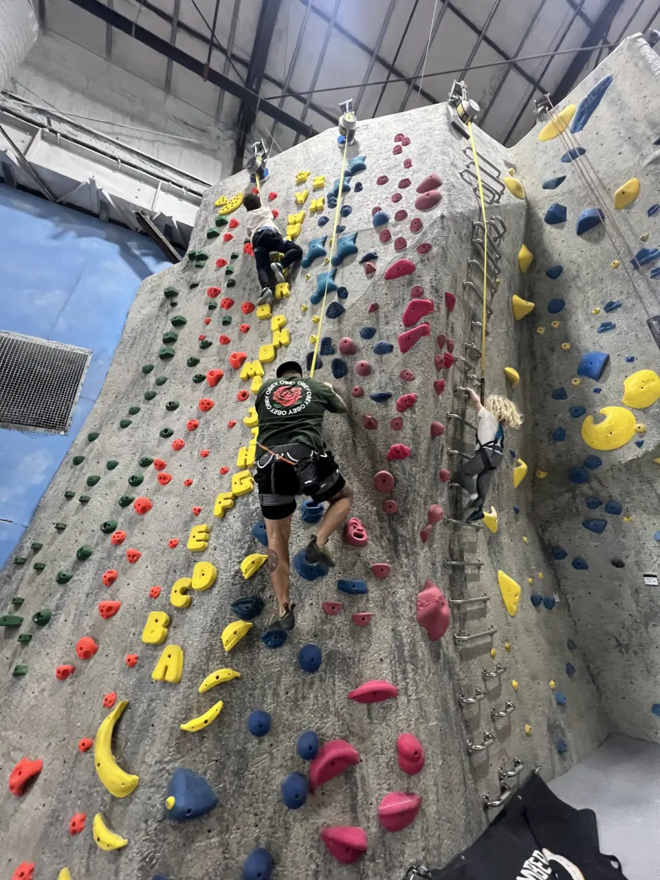 Climbers on a tall top-rope wall with lettered holds