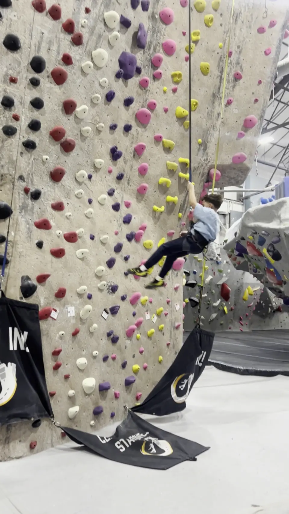 Climber high on a tall wall with an auto-belay at its base