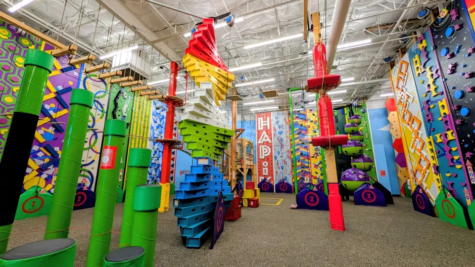 Climbing hall with themed walls, stair towers, green pipe columns and the ropes course above