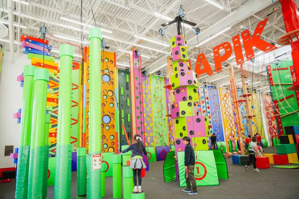 Climbing hall with green pipe columns, a stacked climbing tower and themed walls under the HAPIK sign