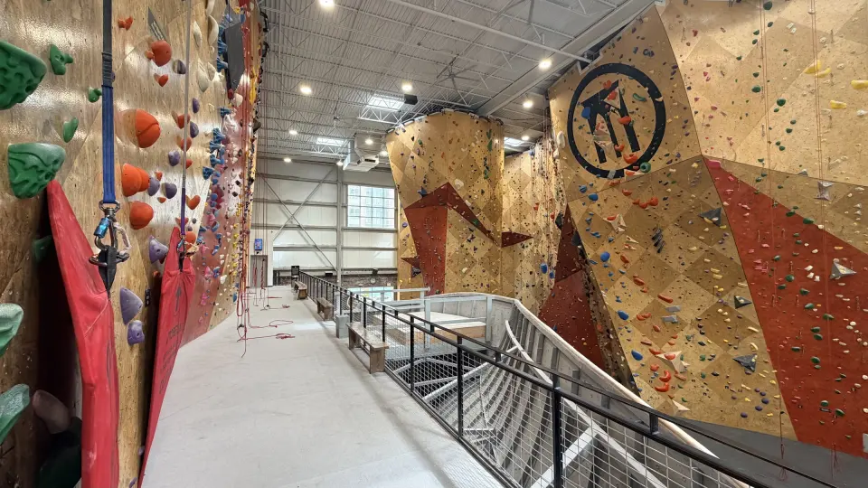 Tall roped walls with the First Ascent emblem beside a ramped walkway