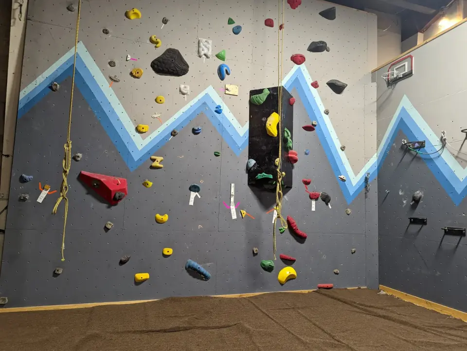 Top ropes hanging on the mountain-painted climbing wall