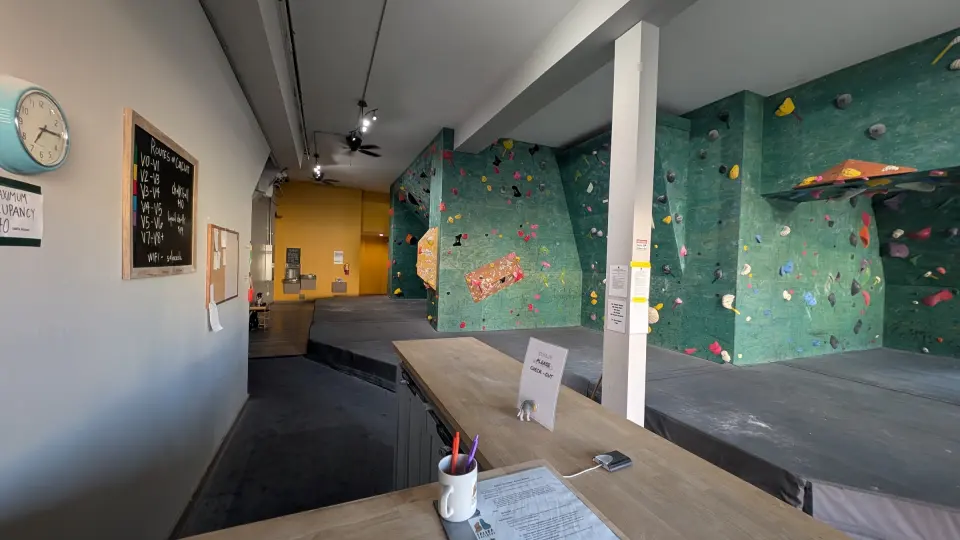 Green bouldering walls and the front desk inside the gym