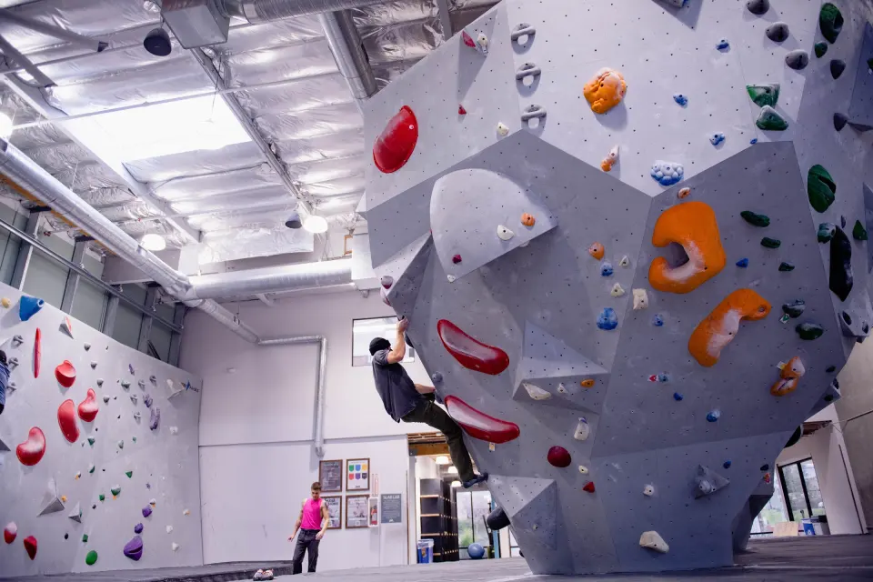 Climber on a grey bouldering wall with big volumes