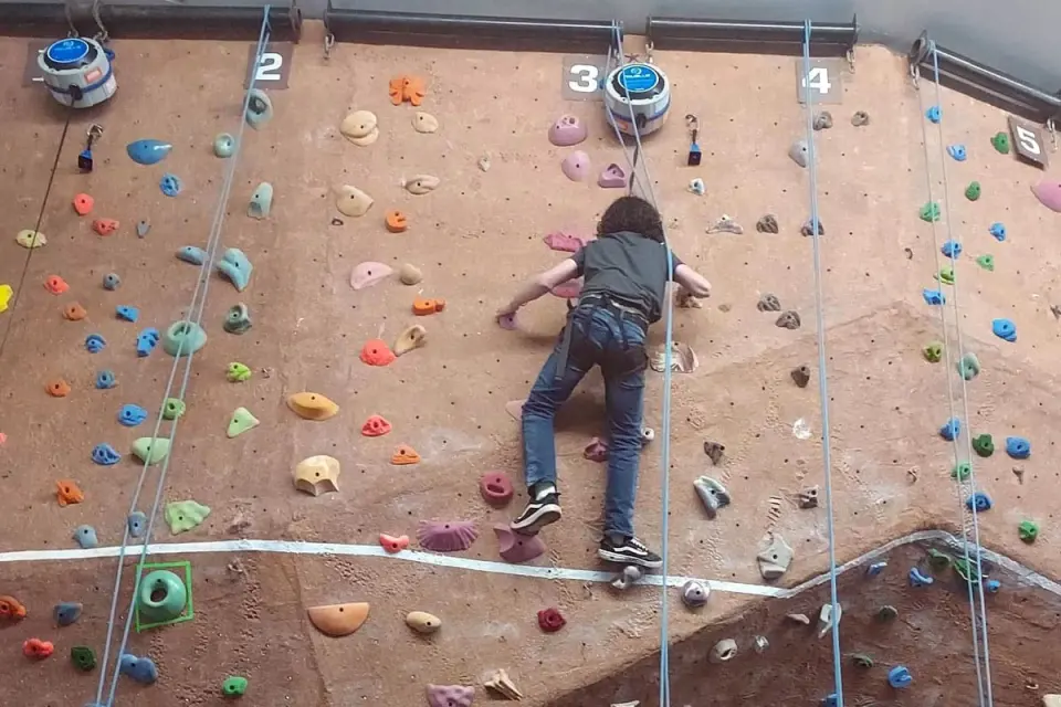 Climber on a top-rope lane of the textured climbing wall, with auto belays at the top