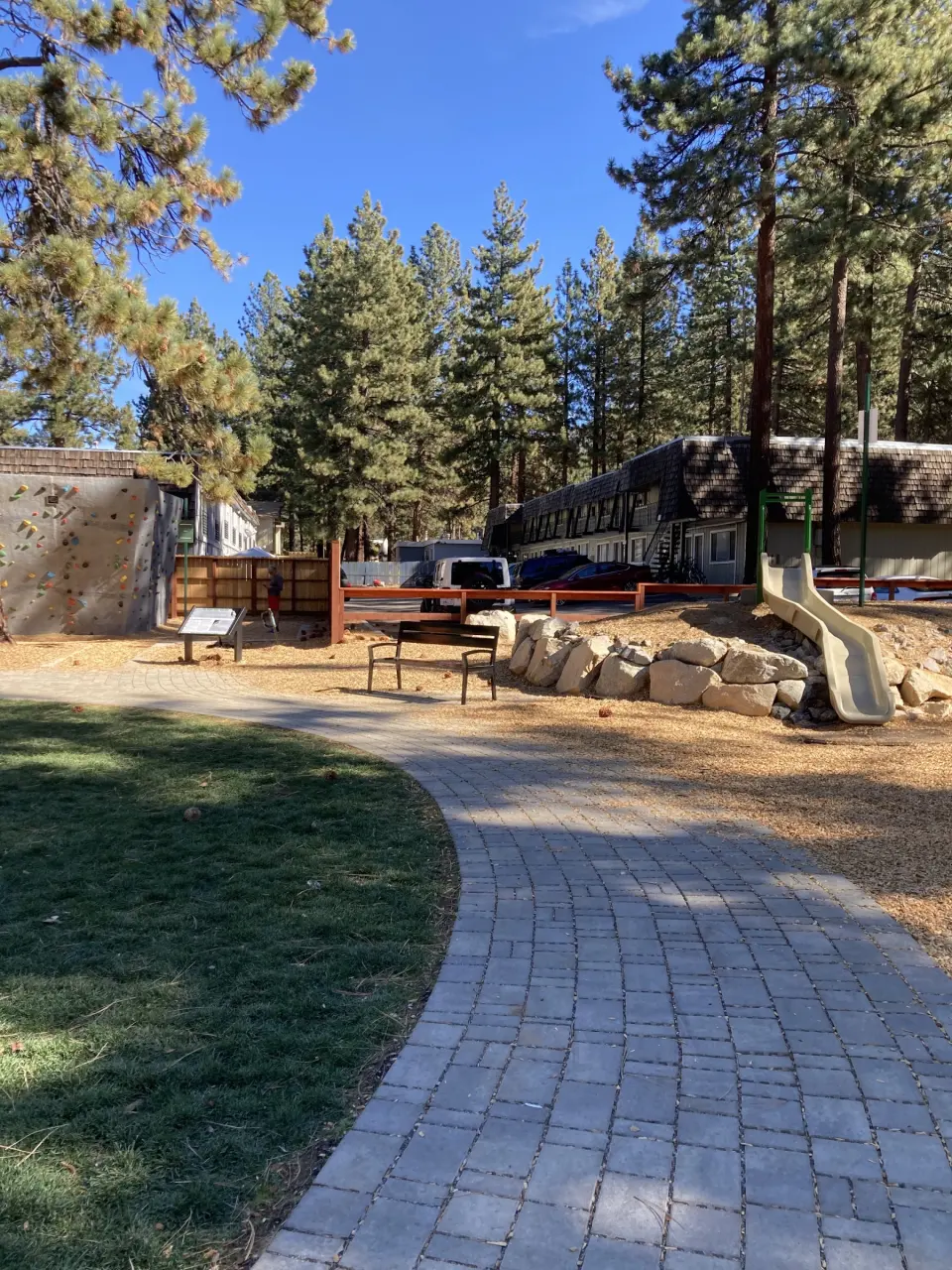 Paved path past the lawn and picnic tables, with the climbing boulder on the left