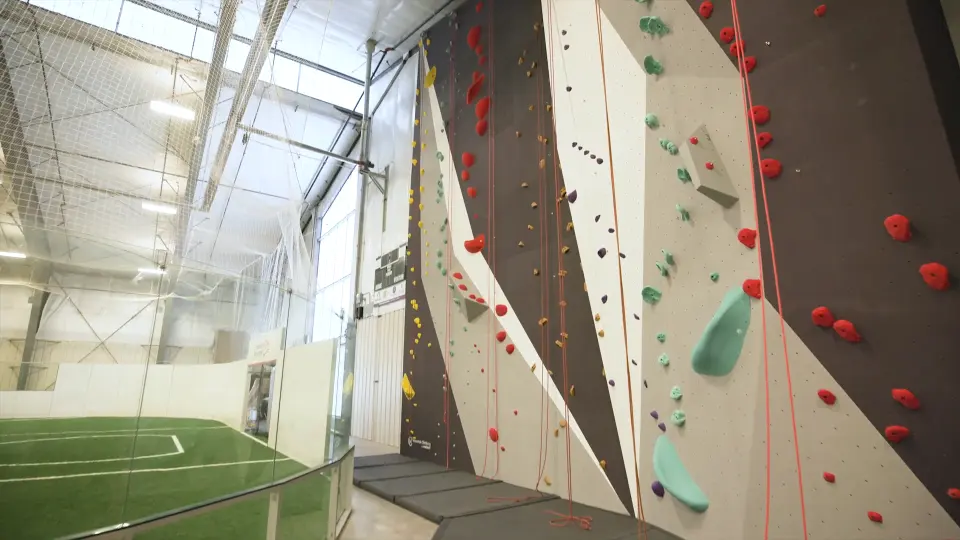 Roped climbing wall beside the glass screen to the indoor turf field