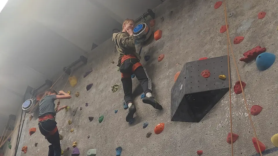Young climbers on the grey roped wall beside a large box volume