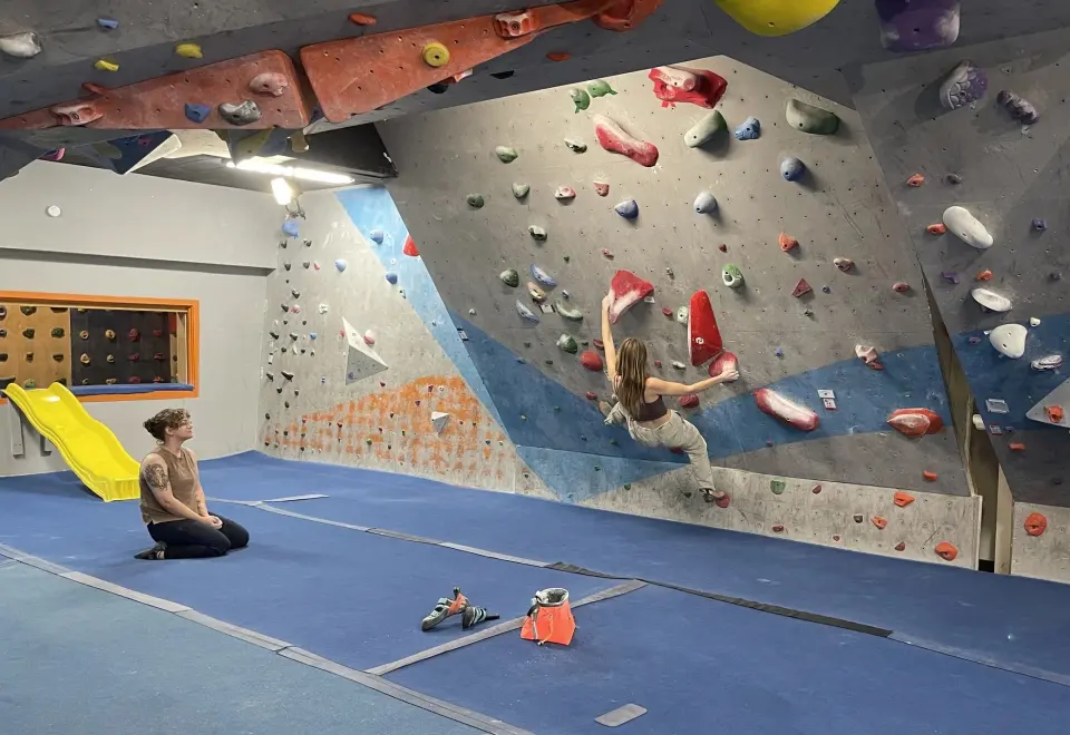 Climber on the grey and blue wall of the main bouldering room, beneath an overhang