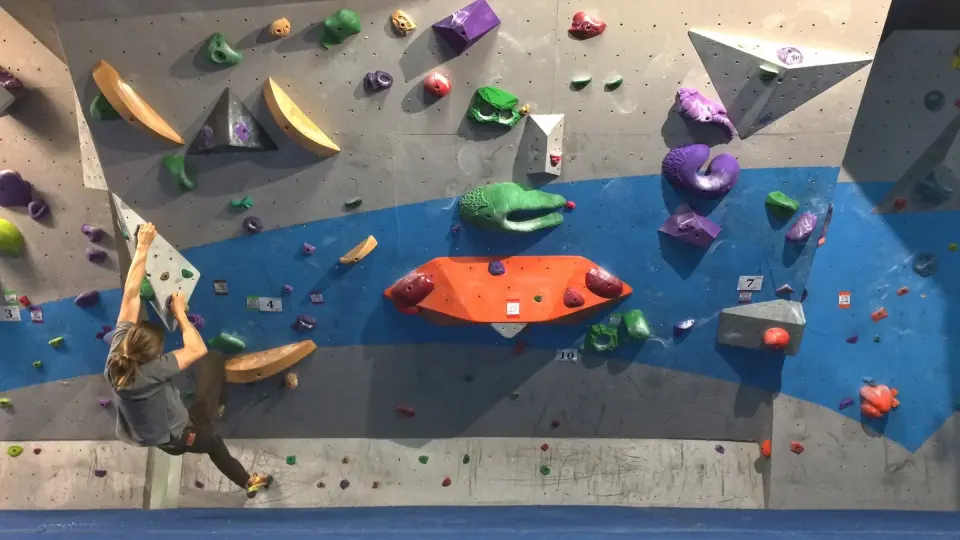 Climber on a grey wall with a blue band and big coloured volumes