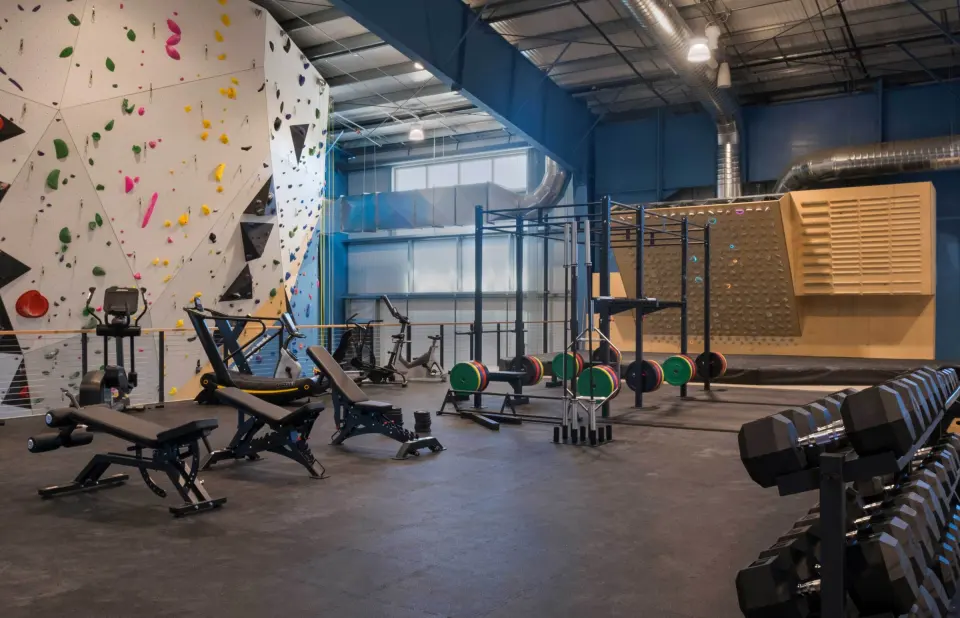 Weights area with racks and benches beside a bouldering wall
