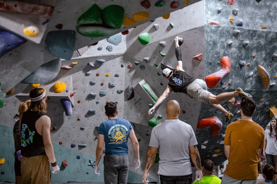 Climber on an overhanging boulder as others watch in the bouldering area