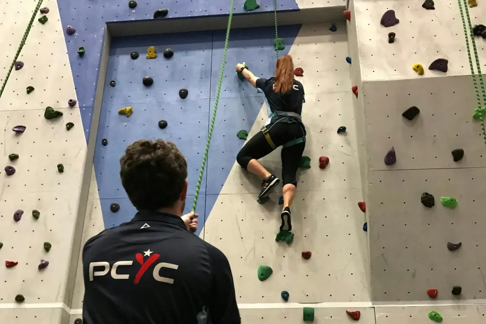A climber on the tall top-rope wall while a PCYC instructor belays below