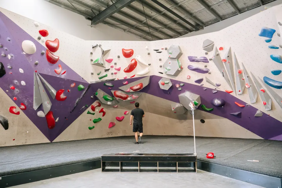 Purple and white bouldering wall with angled volumes above thick crash mats