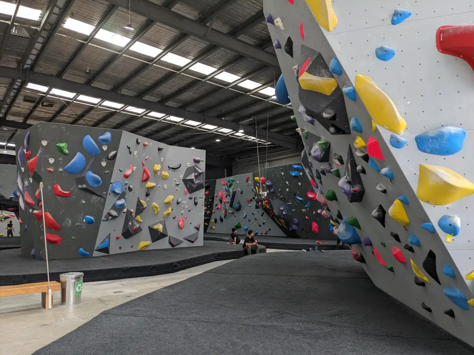Grey bouldering walls with black volumes above dark matting in the main hall