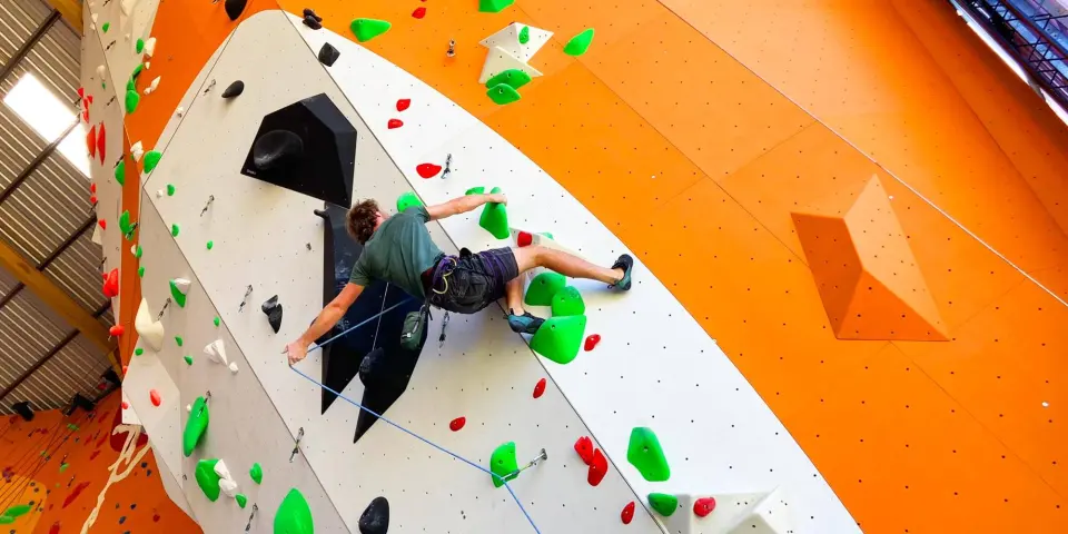 Climber on an overhang on the orange and white rope walls