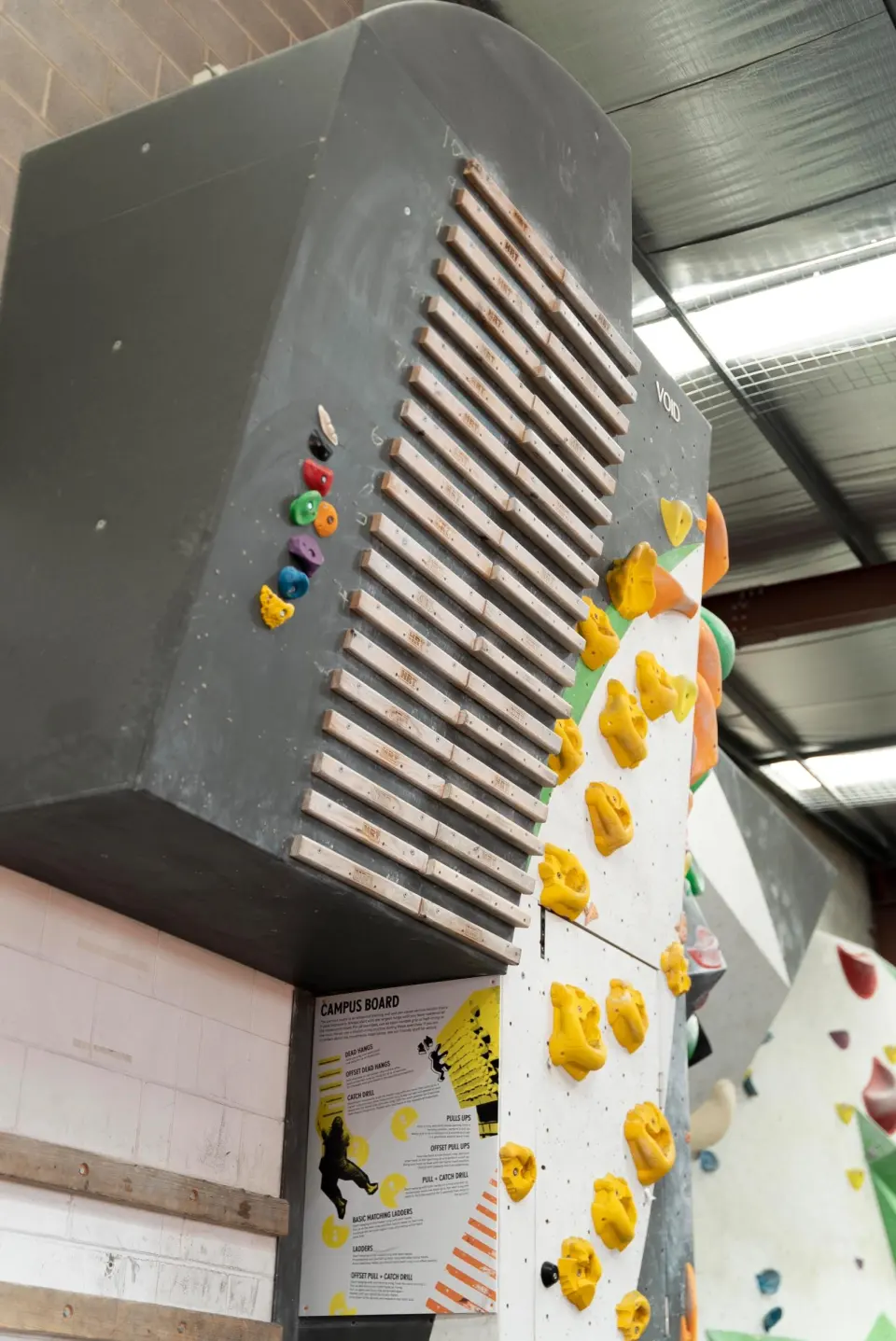 Campus board rungs on a steep wall beside a yellow circuit