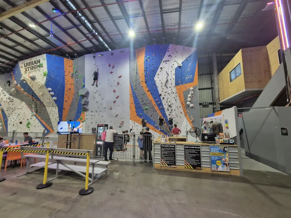 Orange, blue and grey roped walls with climbers and the climbing desk below