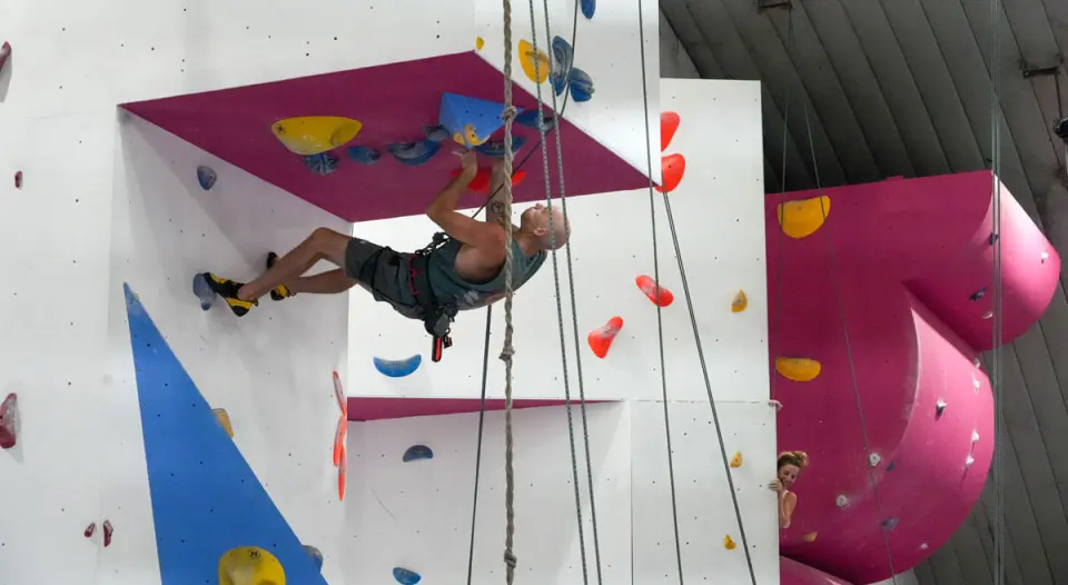 Climber on the overhanging wall beside the pink volumes