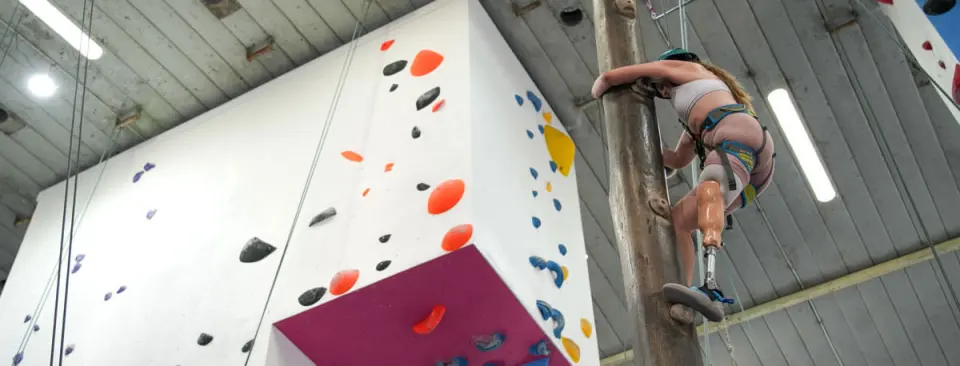 Climber on the wooden climbing pole next to a white wall