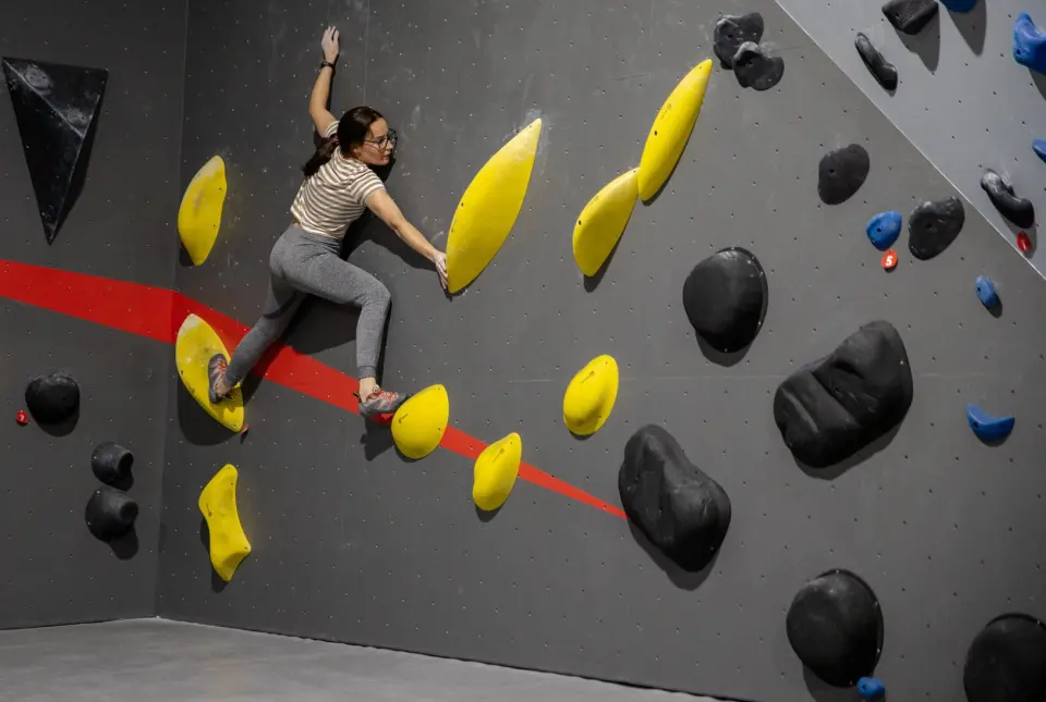 Climber moving between yellow holds on the dark grey wall