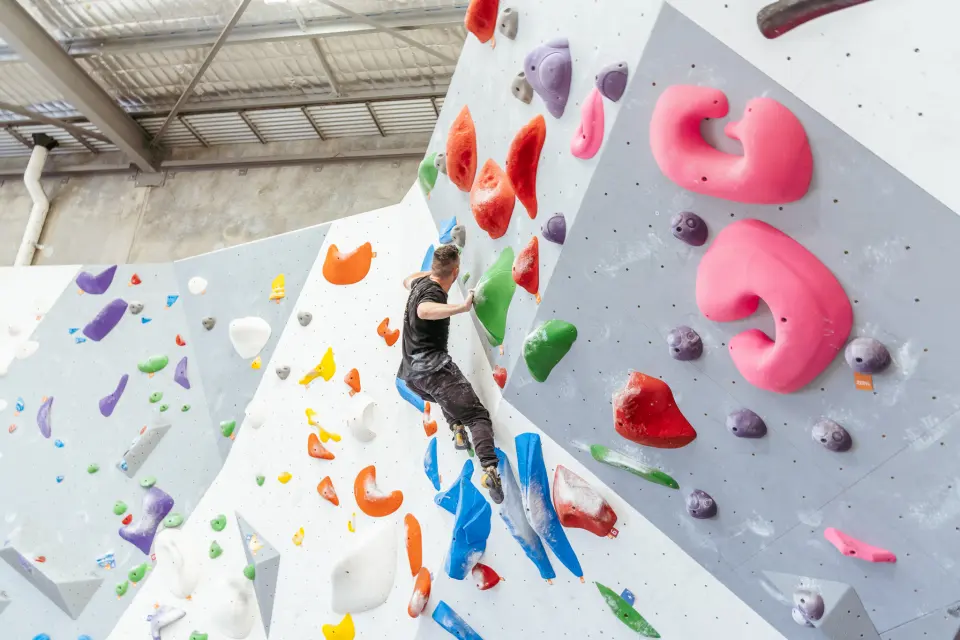 Climber on big pink holds on an overhanging boulder
