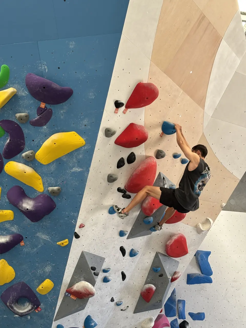 Climber on red holds on a steep blue and beige wall
