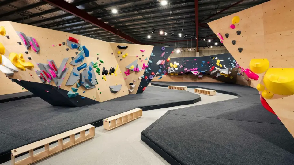 Timber and charcoal bouldering walls above wide black matting in the climbing hall