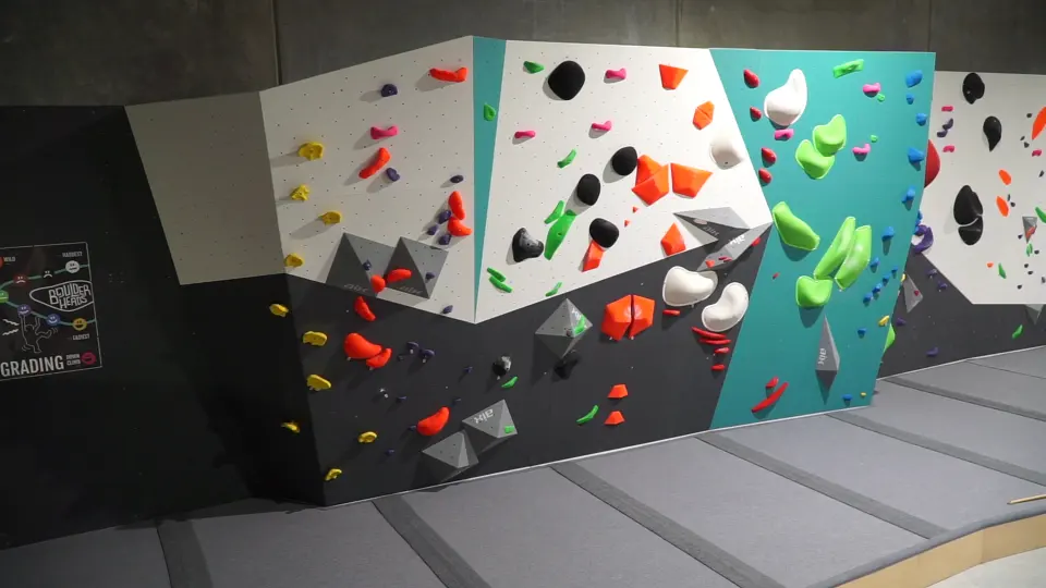 Bouldering wall with teal and white panels above grey matting