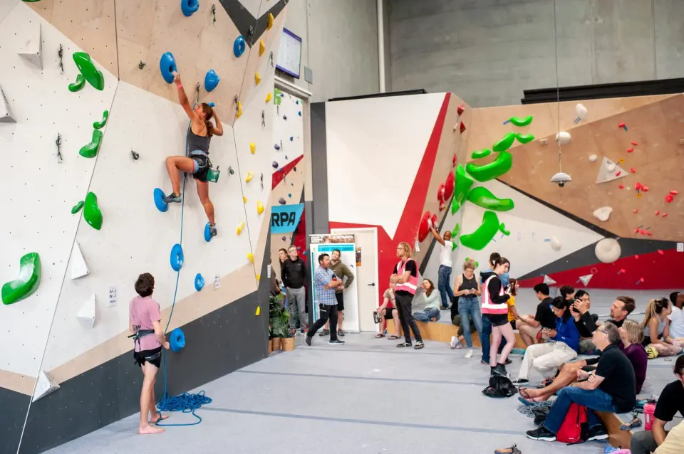 Climber on a roped wall during a competition, with spectators