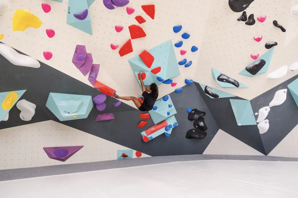 Climber among teal volumes on a cream and grey wall