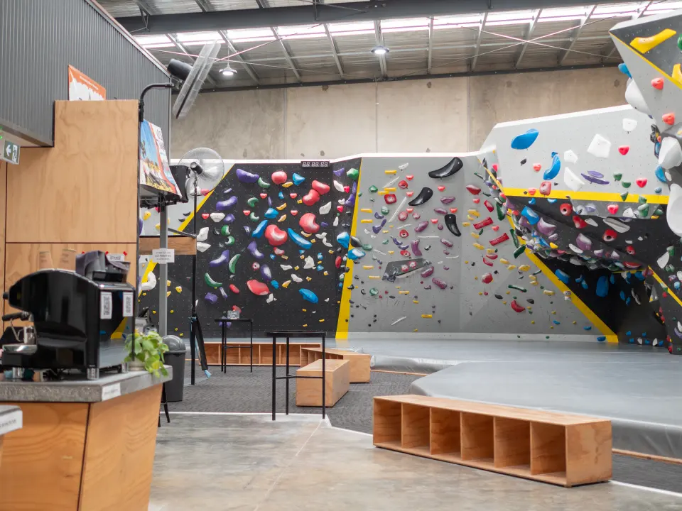 Bouldering walls in grey and black with yellow edging, seen past the café counter