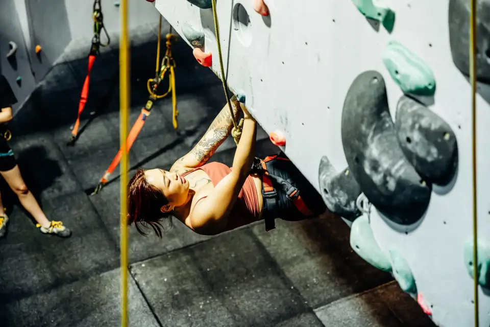Climber on a rope pulling round an overhang on the grey roped wall