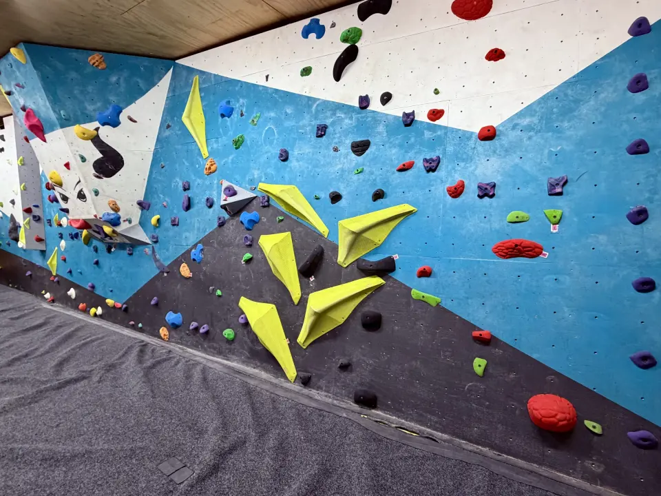 Bouldering wall with yellow volumes and colourful holds above grey matting