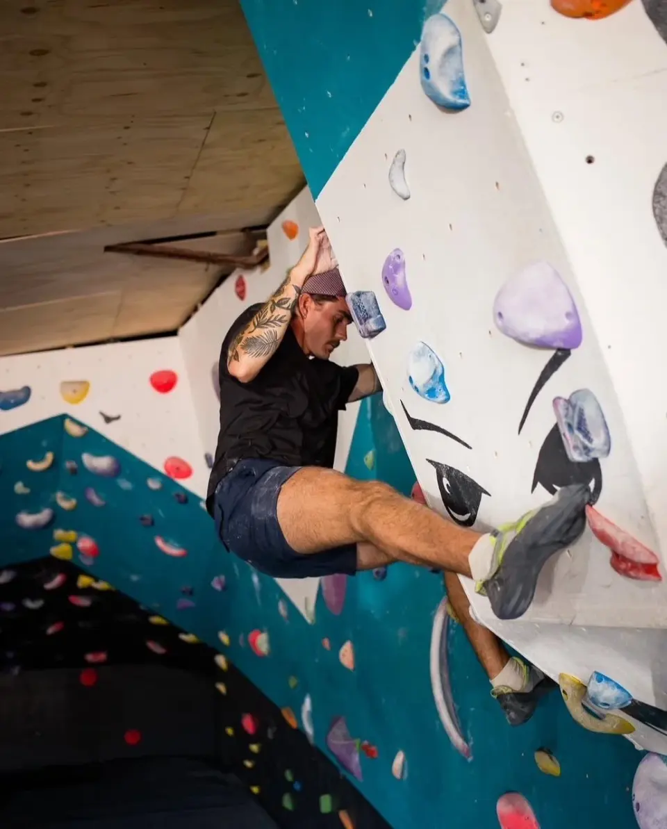 Climber working up the white and teal wall with a painted face