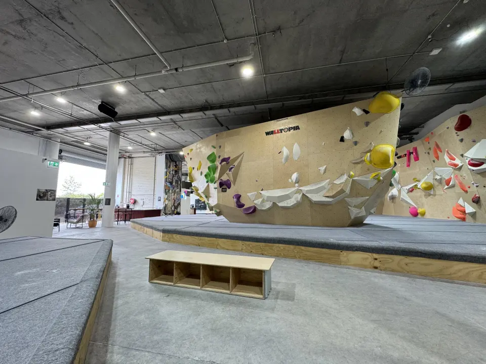 Plywood bouldering walls above a raised matted floor, with a bench in front