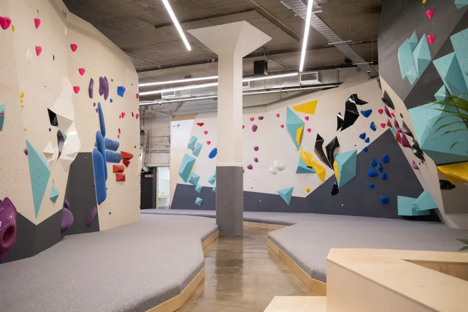 Bouldering hall with cream and grey walls, teal volumes and grey matting