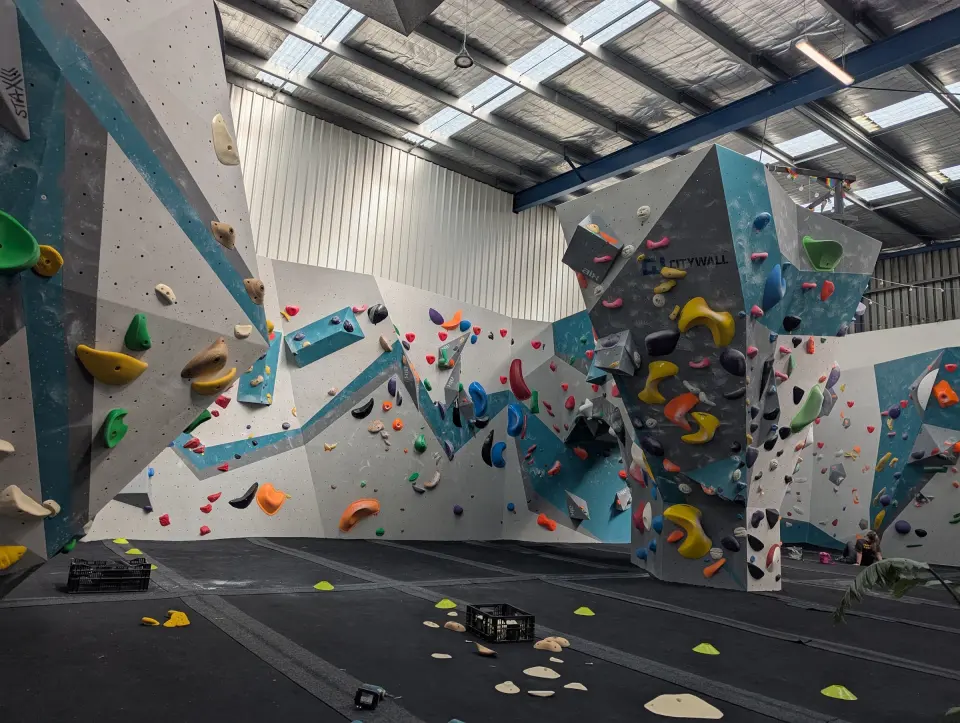 Bouldering walls with teal and grey volumes under the warehouse roof