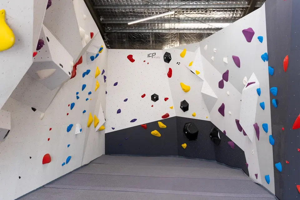 Bouldering walls with coloured holds and volumes around a corner of the matted hall