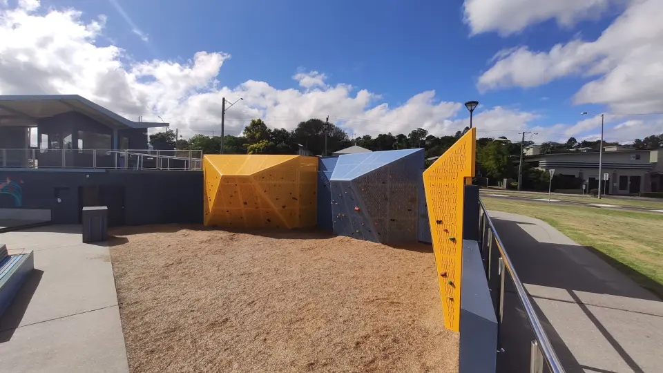 Yellow and blue steel bouldering blocks over soft-fall mulch beside the precinct pavilion