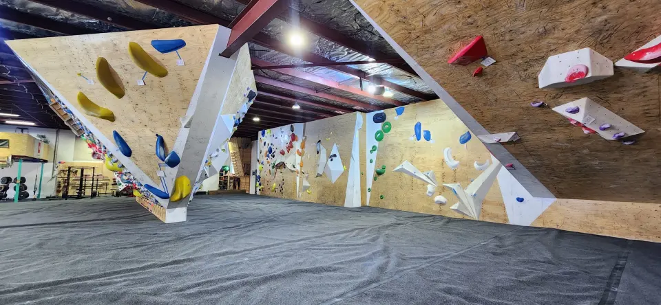 Bouldering hall with an overhanging prow, coloured holds and dark matting
