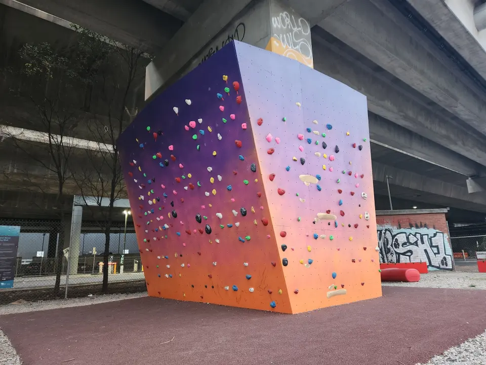 Purple-to-orange bouldering block covered in holds, wrapped round a freeway pier