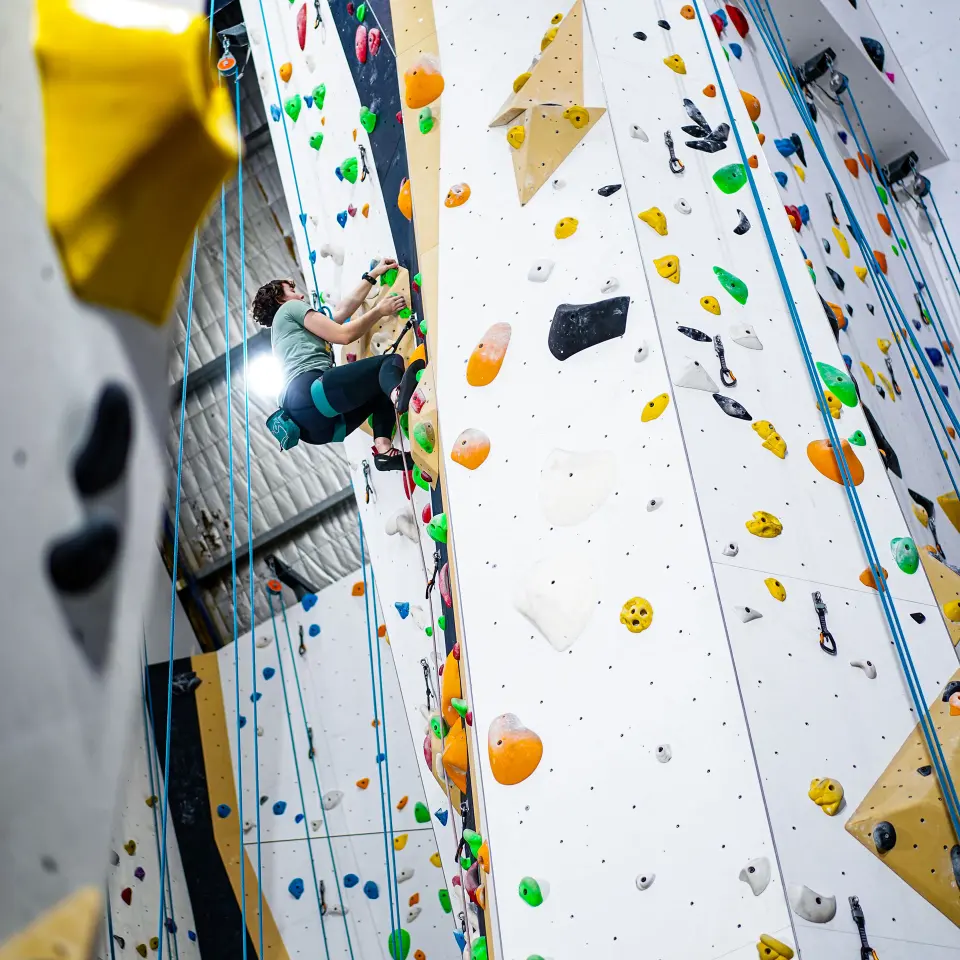 Climber high on a tall wall lined with ropes