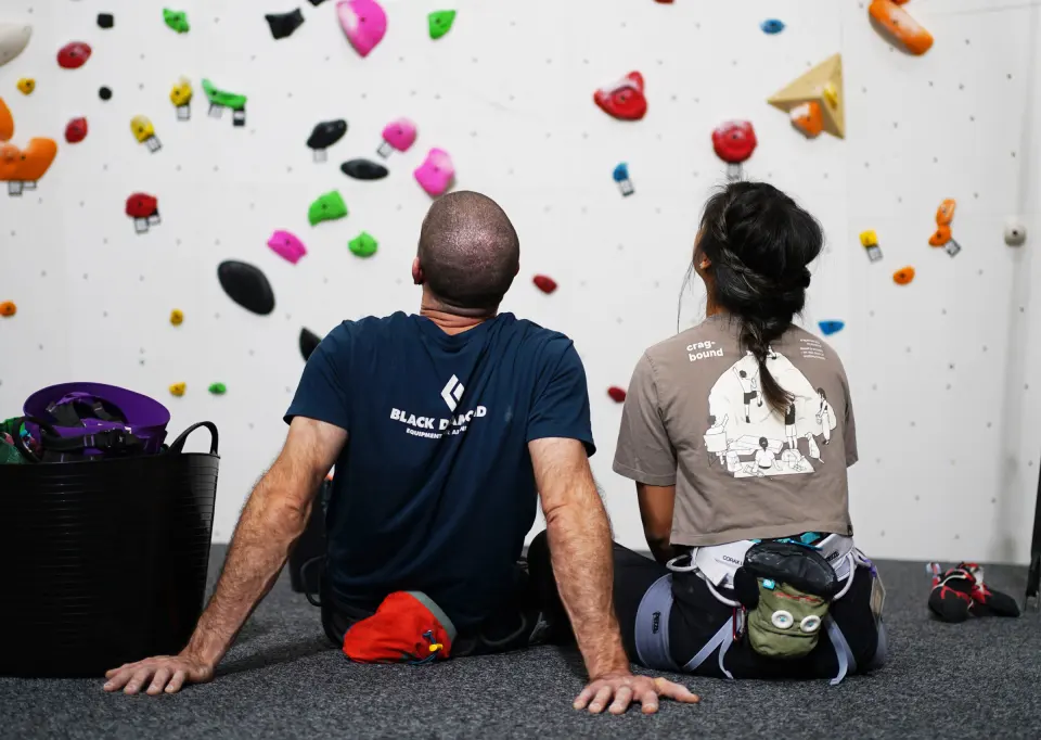 Two climbers sitting on the mats studying a wall of holds