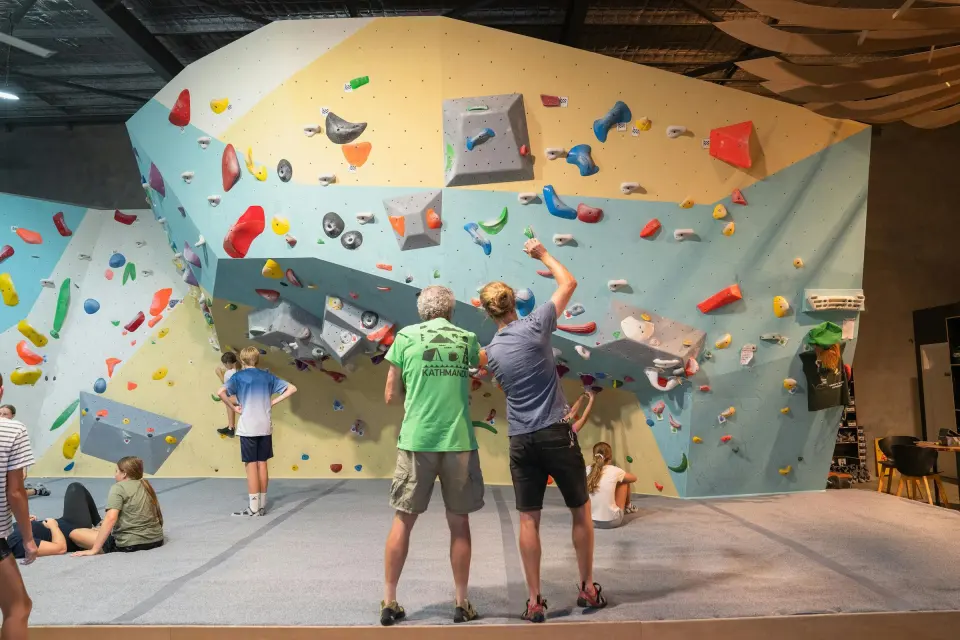 Climbers studying the main bouldering wall and its grey volumes