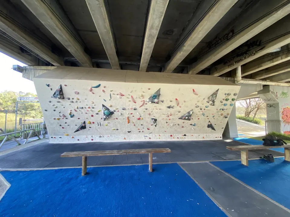 Overhanging bouldering wall beneath the freeway deck, with benches on blue matting